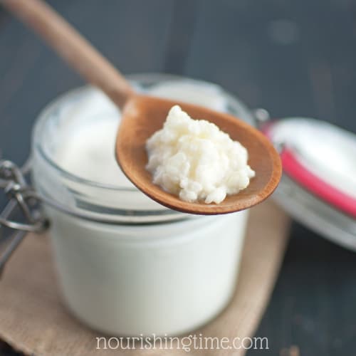 Coconut Milk In Small Clamp-style Jar With a Spoon Of Milk Kefir Grains Above It